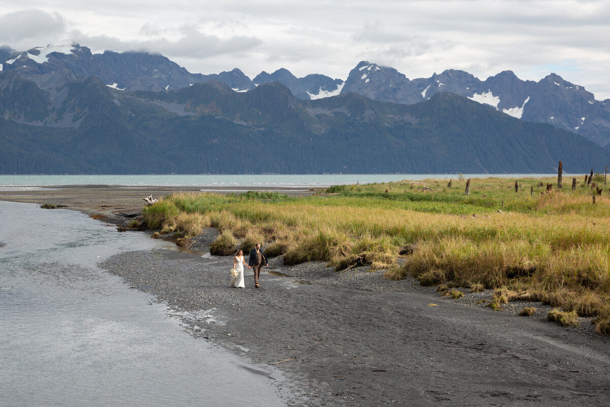 A bride and groom walk along a black sandy beach in Alaska on their elopement day.