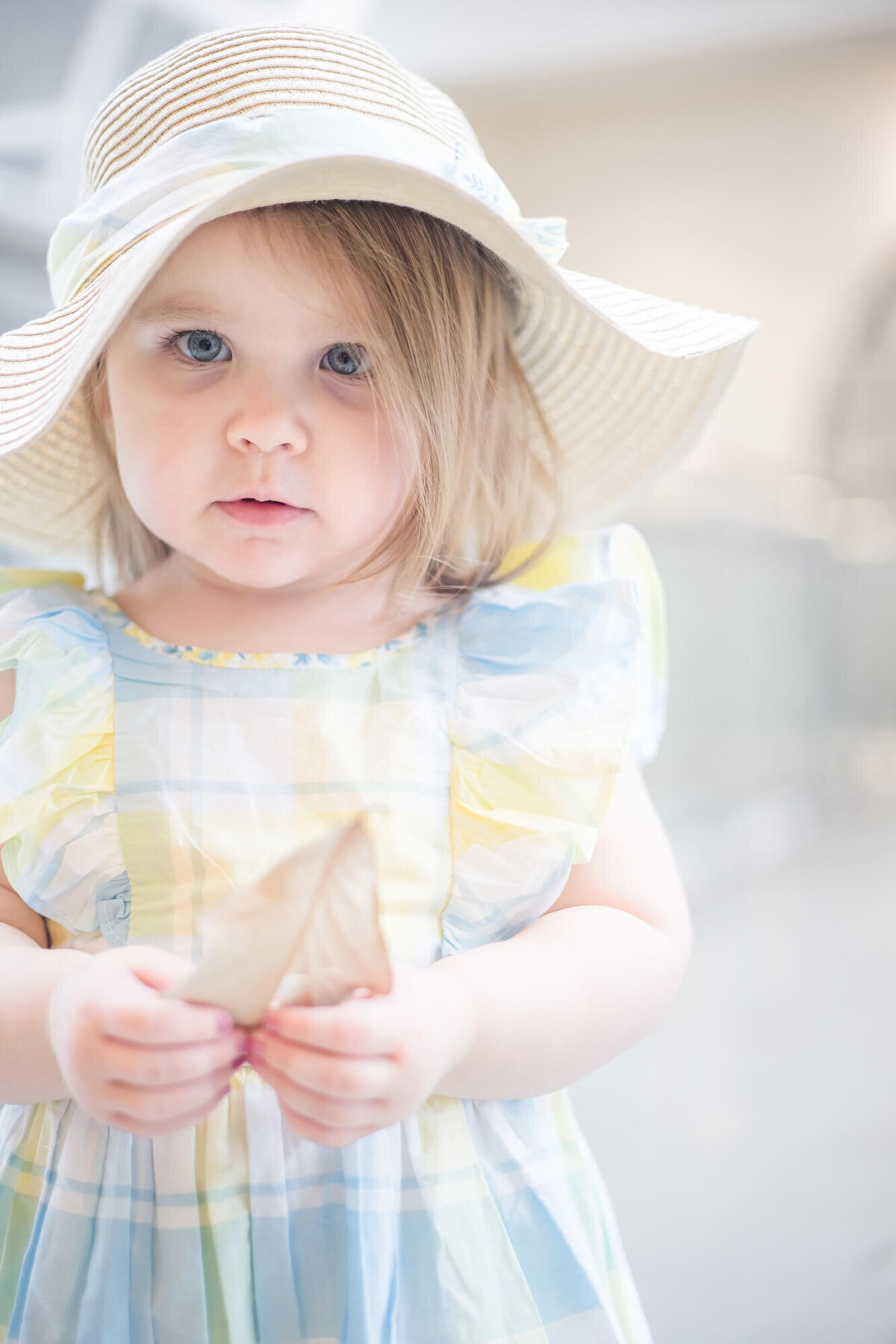 2 year old toddler girl in a sunhat  ;looking intently with a leaf in her hand