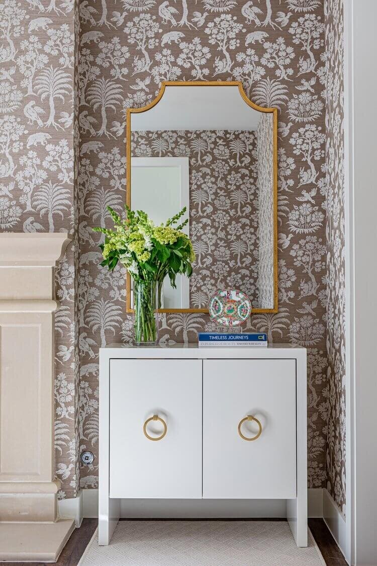 oyster creek studios highland park home white accent table with gold mirror and fresh flowers in room with taupe floral wallpaper