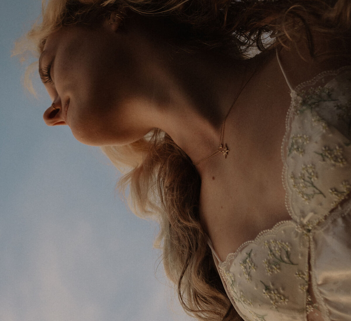 close up of woman with blonde hair and a white dress standing against a blue sky backdrop
