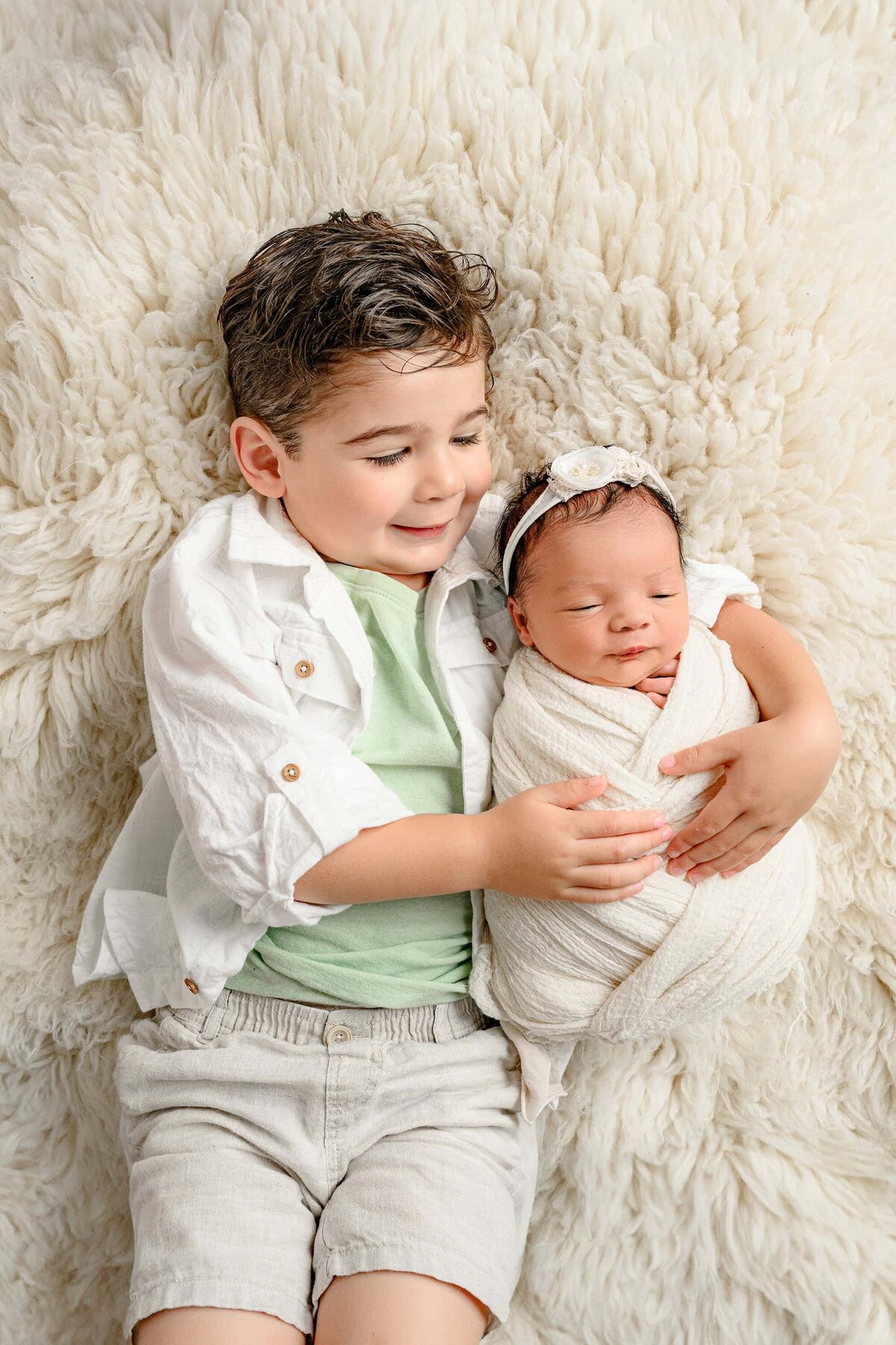 little boy snuggled his newborn baby sister on a furr rug