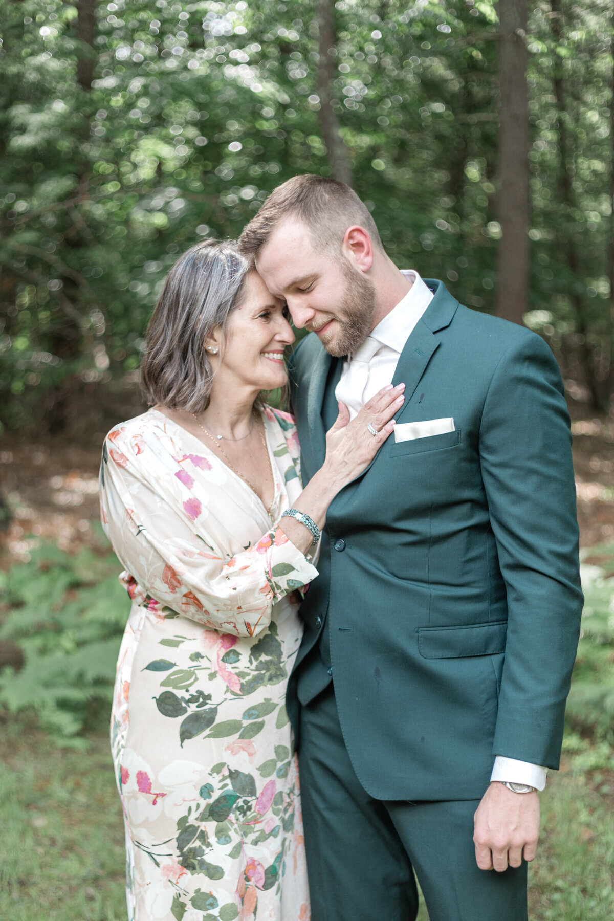 A groom in a dark green suit hugs his mother