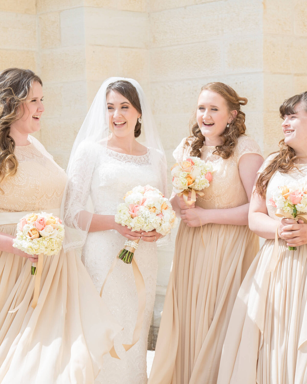 bright wedding photography of bride in lace dress  laughing  with bridesmaids holding bouquets