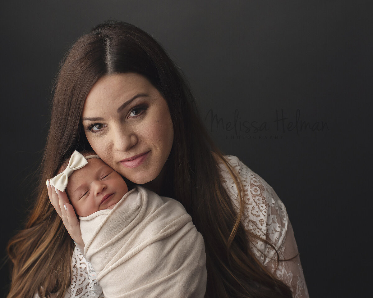 Mom looks at camera while holding daughter with bow in her hair