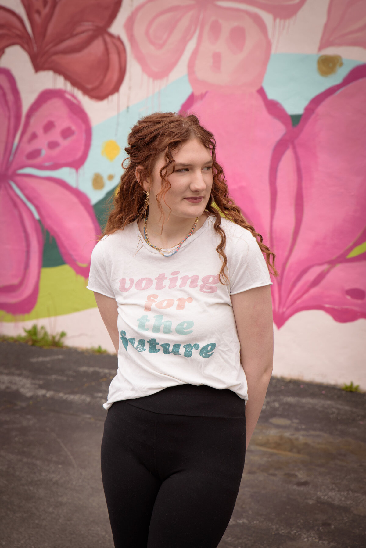 Green Bay East High School senior girl wearing a graphic t-shirt and leggings in front of a painted flower mural in an urban setting in downtown Green Bay, Wisconsin