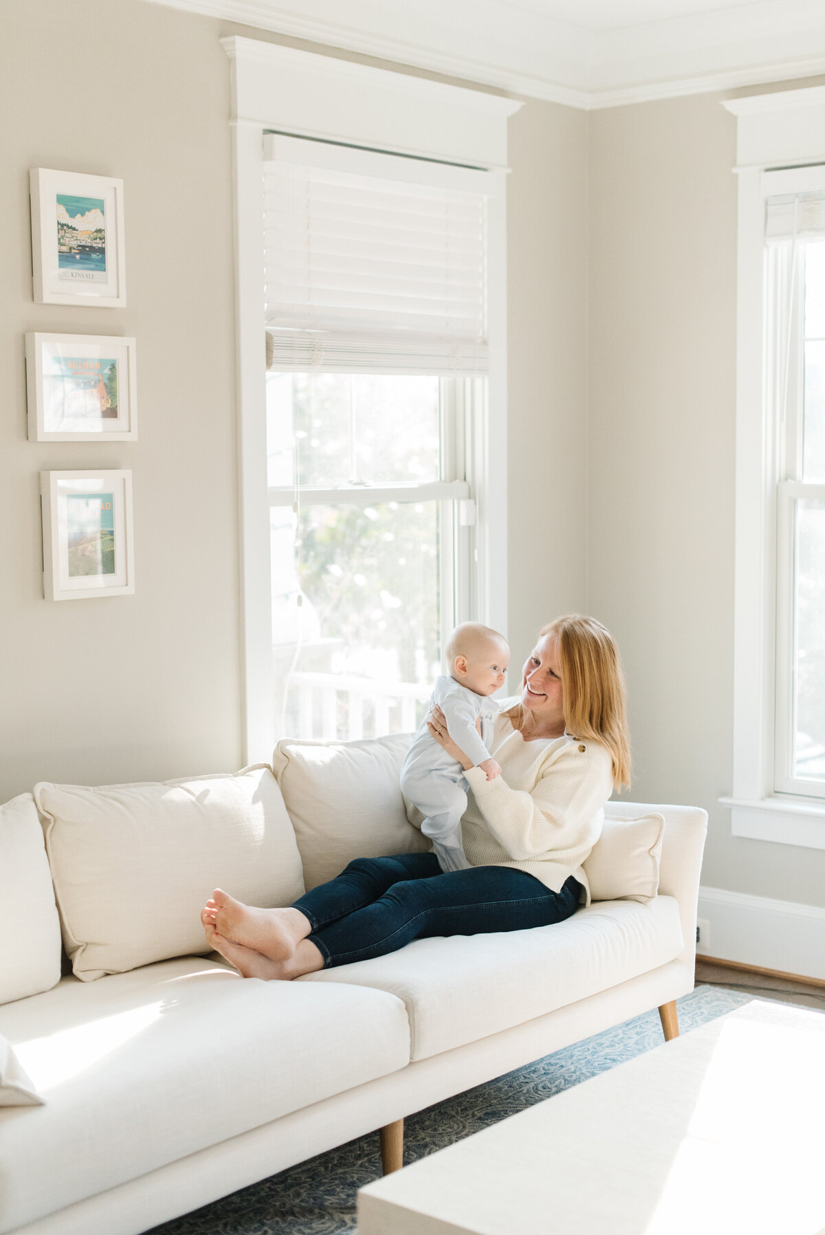 Mother holding baby on white couch and smiling