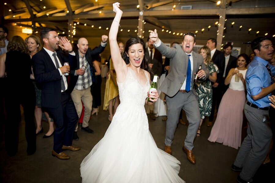 A bride throws a hand into their air as she energetically dances at her wedding reception, captured by Denver wedding photographer, Casey Van Horn.