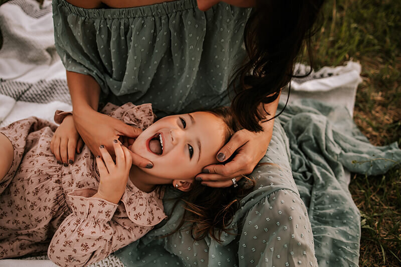 Toddler girl lays on top of moms lap while laughing
