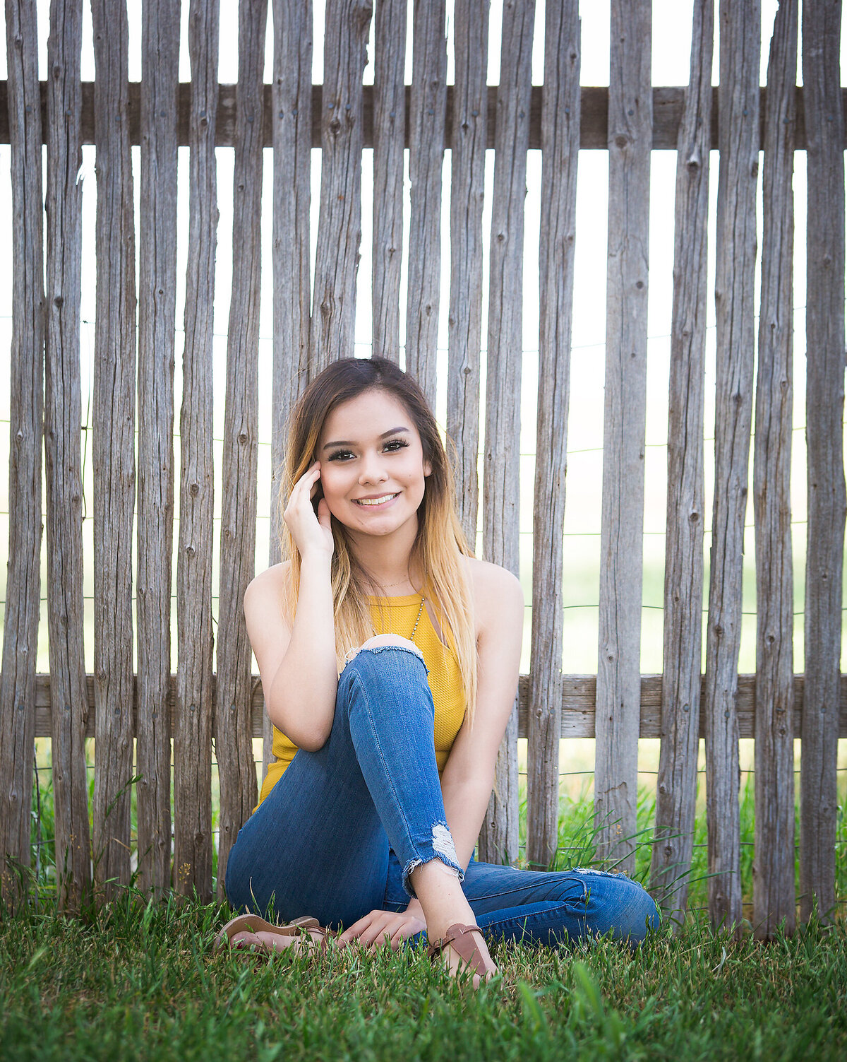 Smiling senior girl sitting next to wooden fence