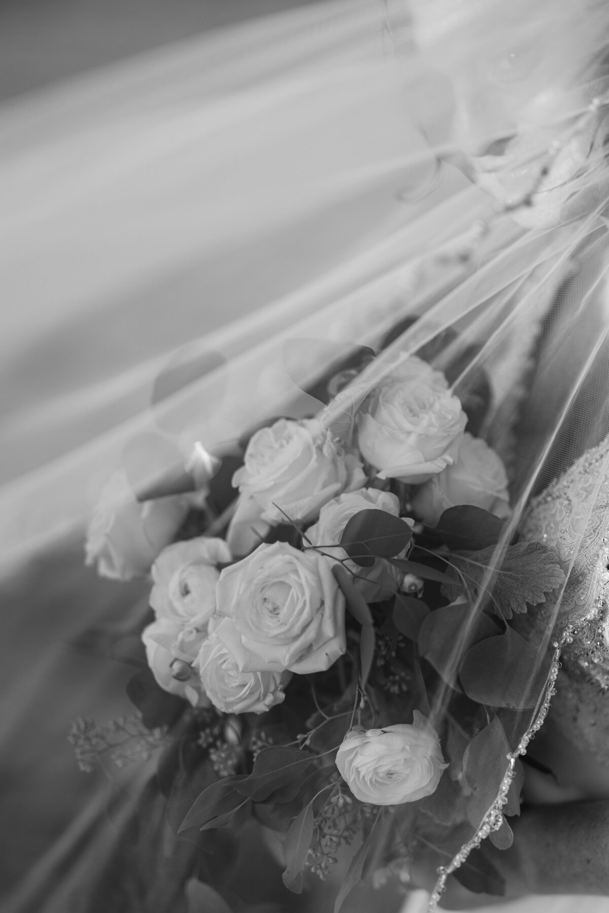 black and white image of bridal bouquet behind veil