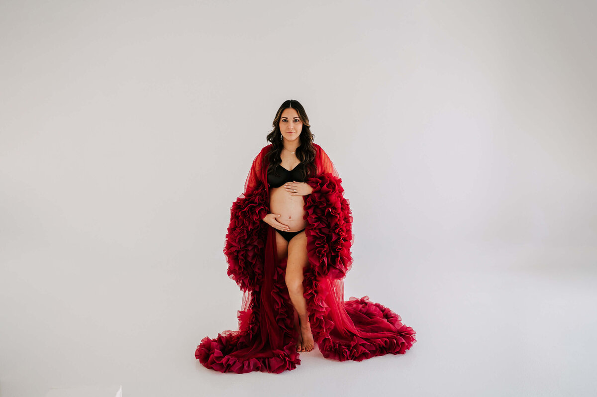 pregnant mom standing holding baby bump in red robe enjoy maternity photography in Joplin MO