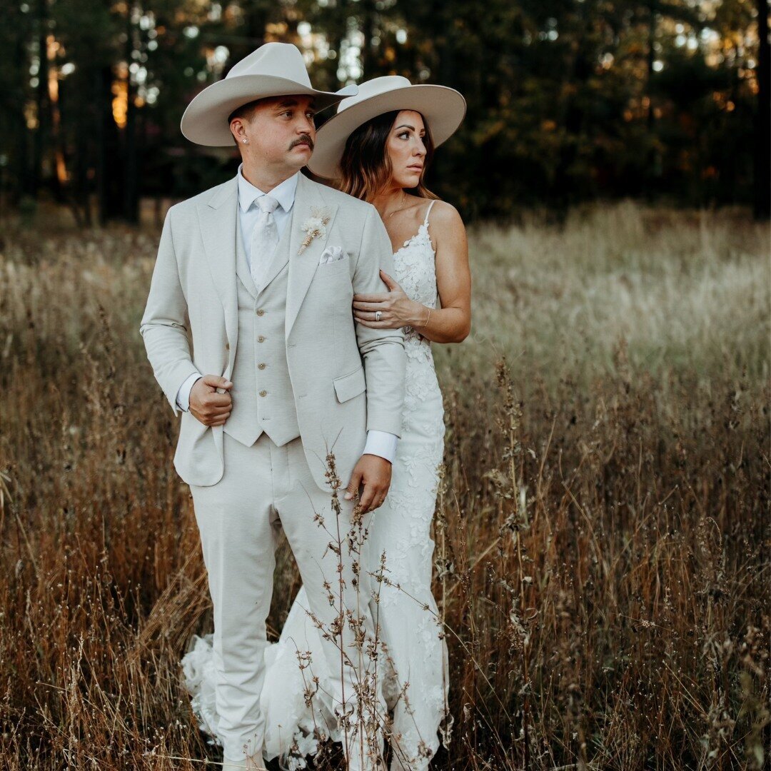 A bride and groom in western wedding attire standing in a field