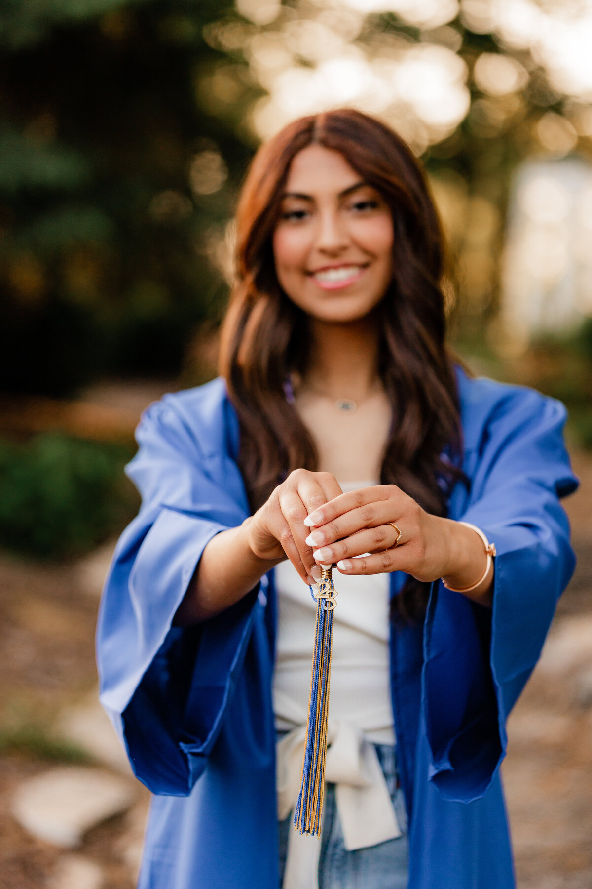 A teen girl poses in her graduation gown holding her tassle at Dellwood Park.