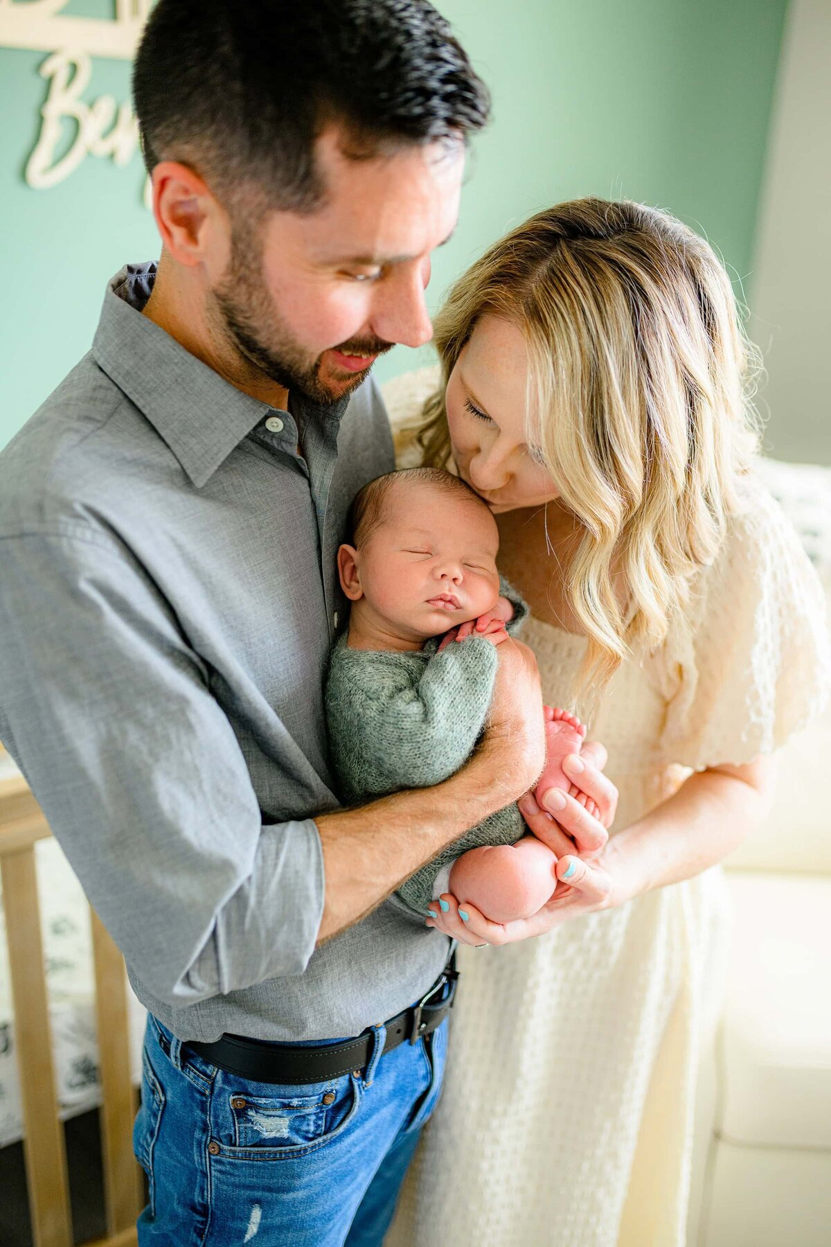father hods his newborn son while mother kisses newborns head