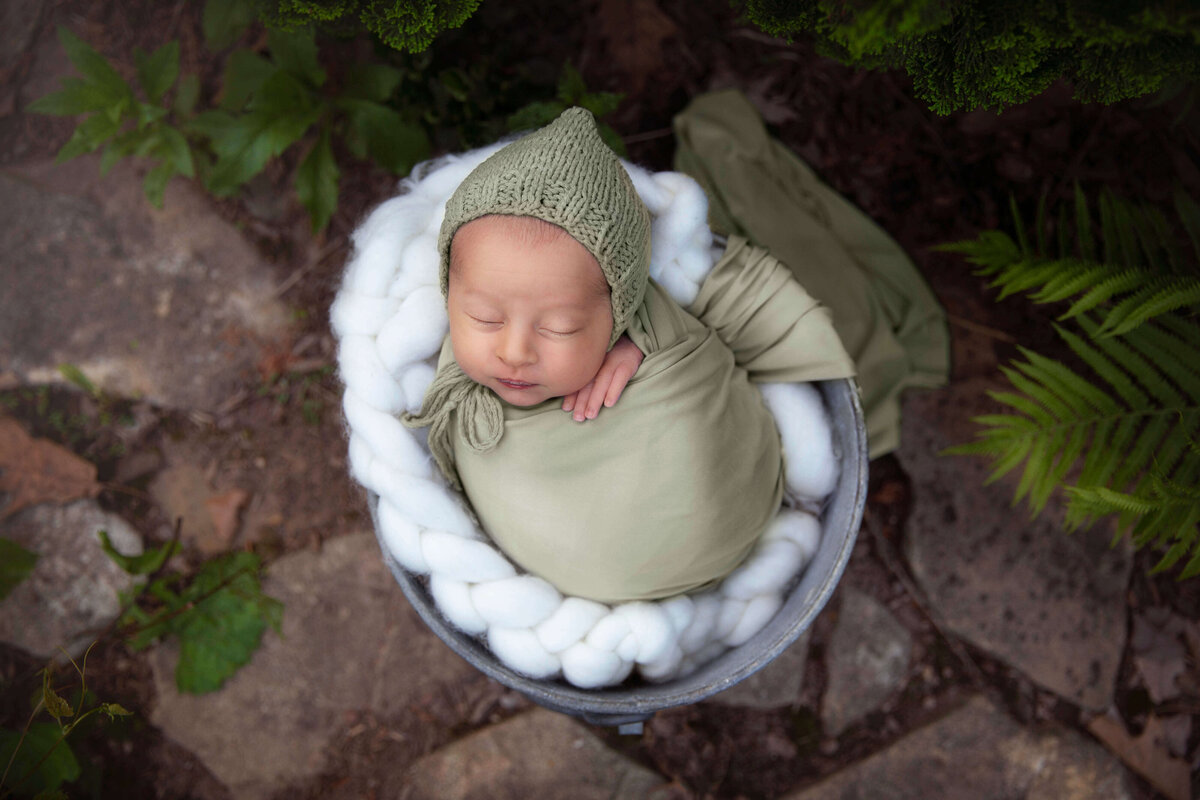 Newborn boy sleeping in bucket outside