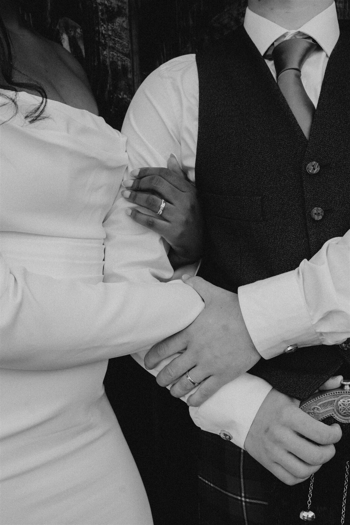 A close photograph of a bride and groom linking arms and hands.