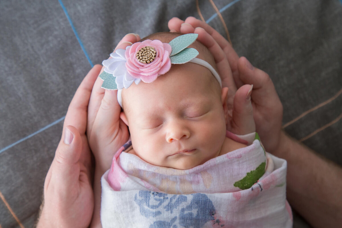 Newborn baby girl sleeping wrapped in a swaddle, held in parents hands