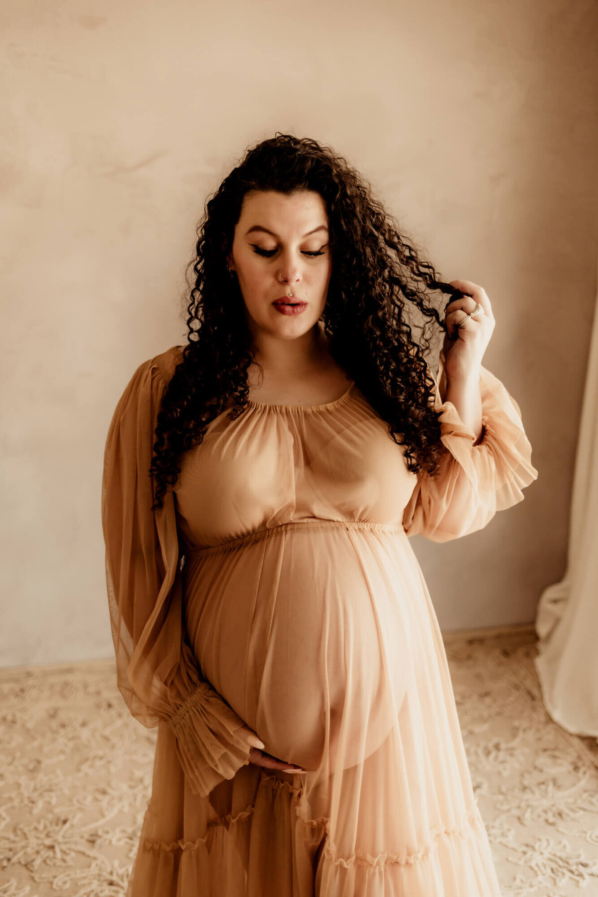 Pregnant woman plays with her hair while looking at her baby bump in OKC.
