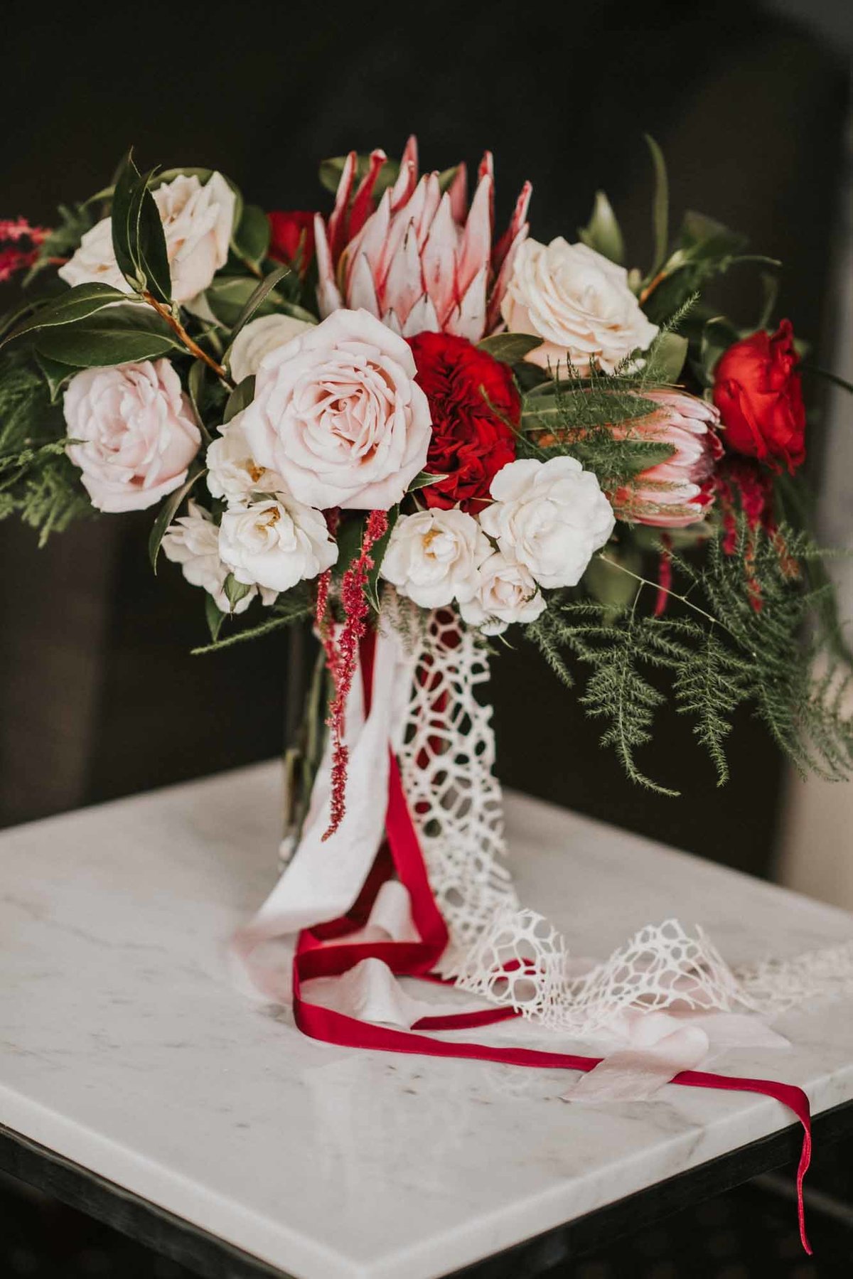 bridal bouquet of winder flowers with pink protea, blush roses, ferns, and long ribbon streamers