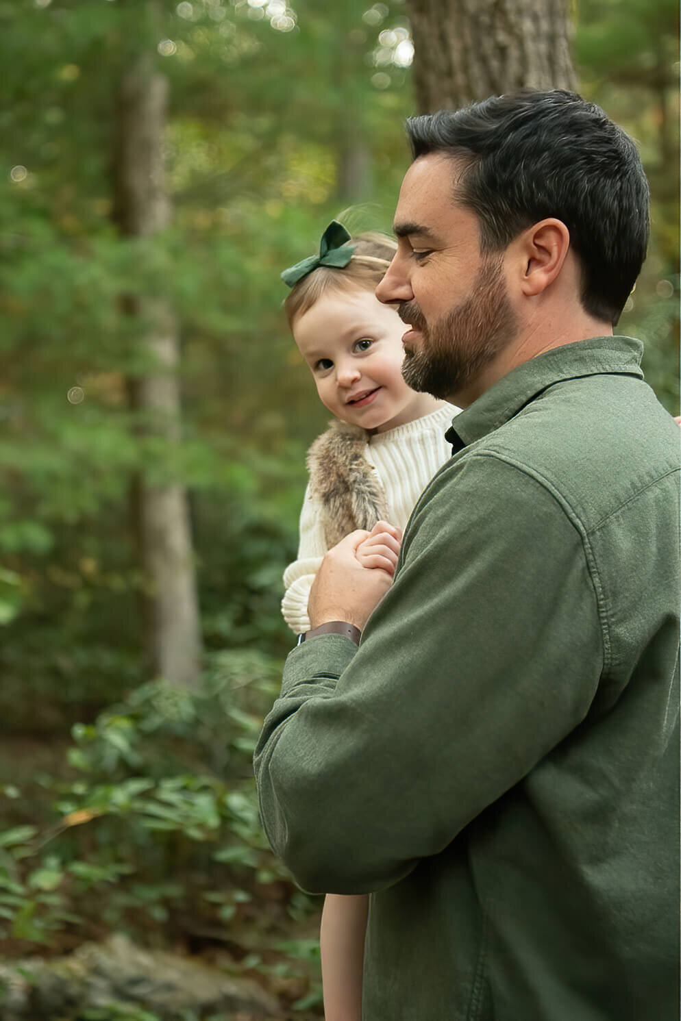 A dad holds his daughter as she smiles at the camera at Whip Hill Park.