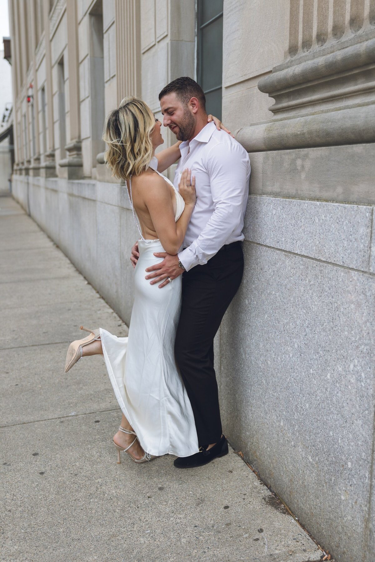 Bride resting her head on groom's shoulder against stone wall.