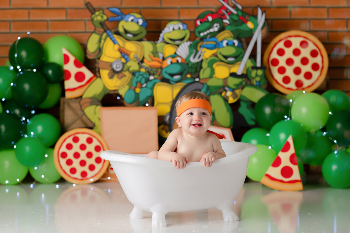 One year old Tampa baby enjoying a personalized luxury cake smash session with playful ninja turtle decorations