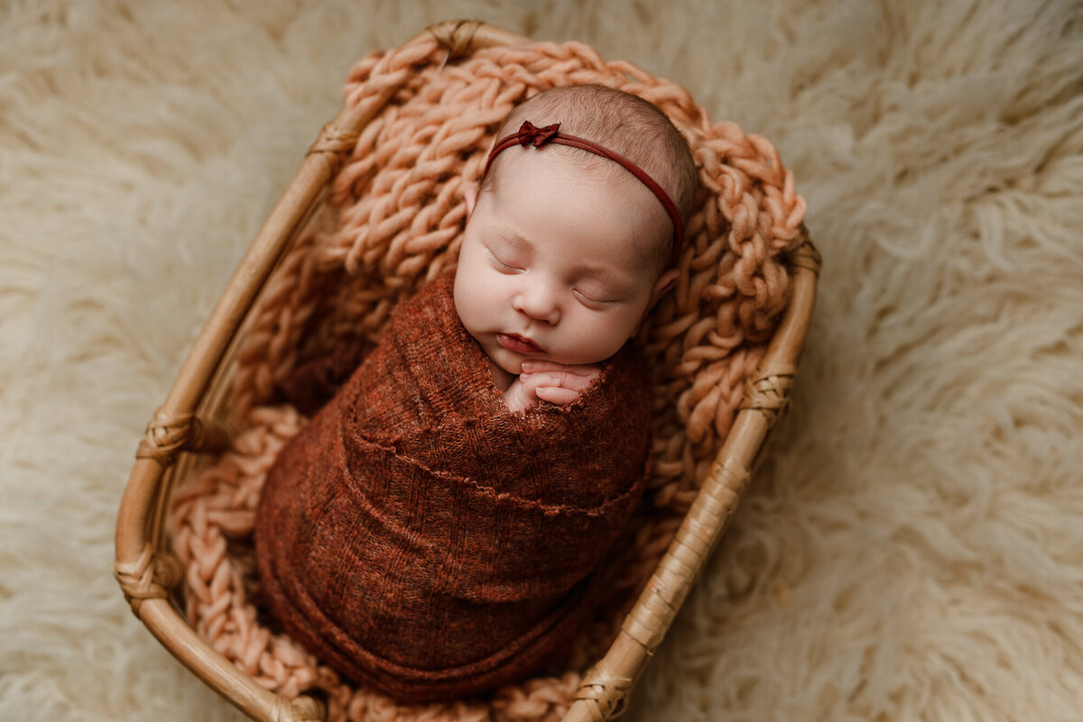 Baby girl wrapped in rust colors on fluffy flokati backdrop