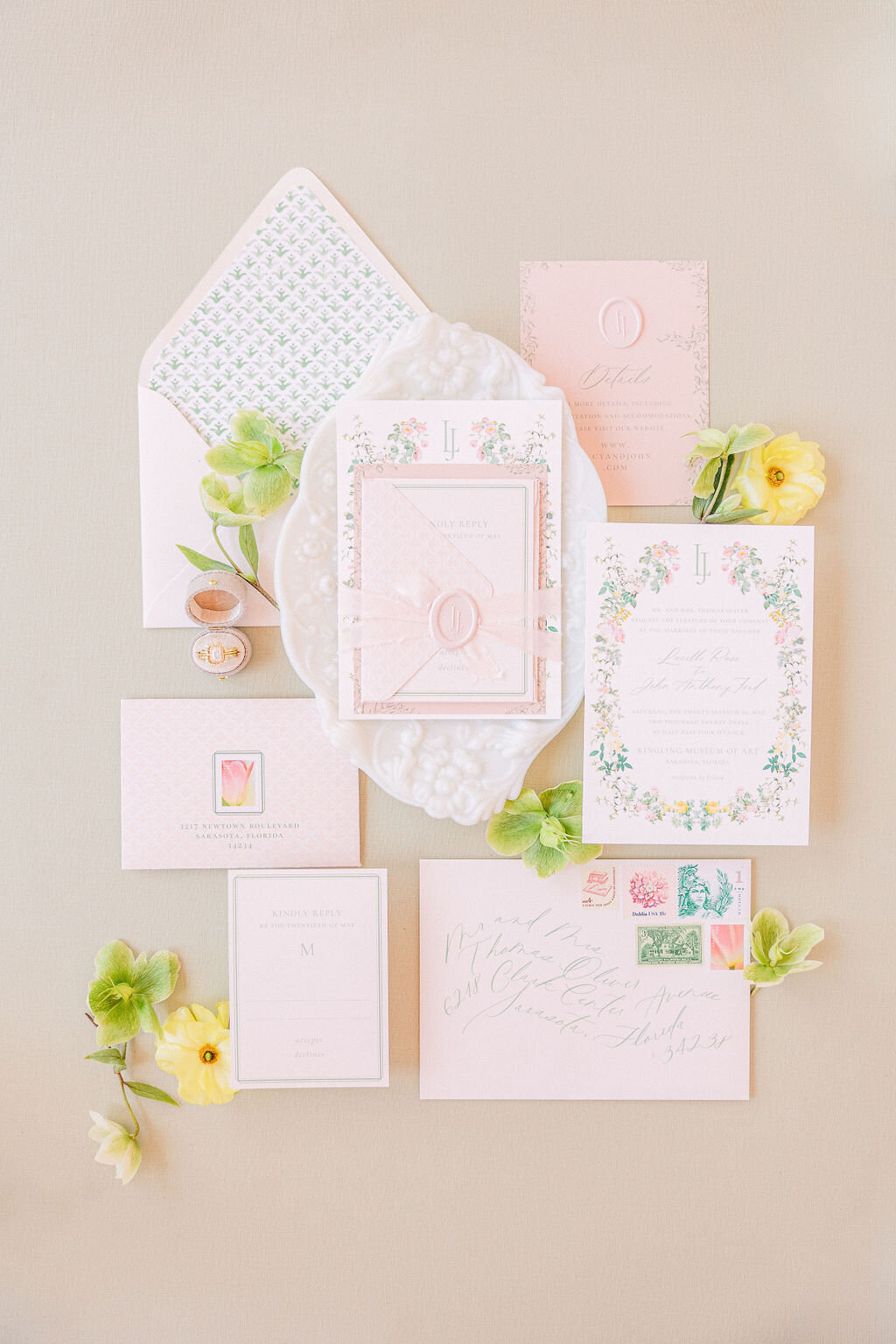 Pastel pink and floral wedding invitation suite with wax seals, vintage stamps, and yellow ranunculus—styled flat-lay for a Ringling Museum wedding in Sarasota, captured by luxury wedding photographer Amia Marcell.