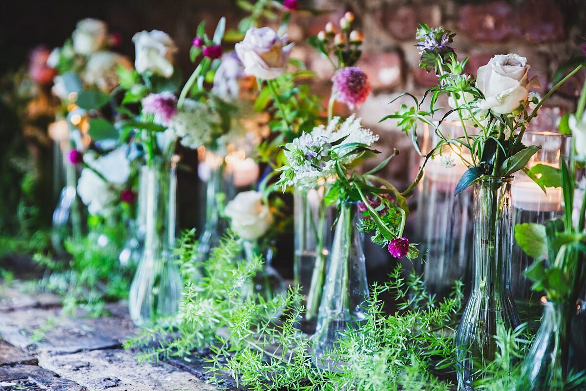 A wedding centerpiece made up from a large collection of bud vases in varying shapes and sizes. The bud vases have an assortment of wildflowers in yellow, pink, white and purple.