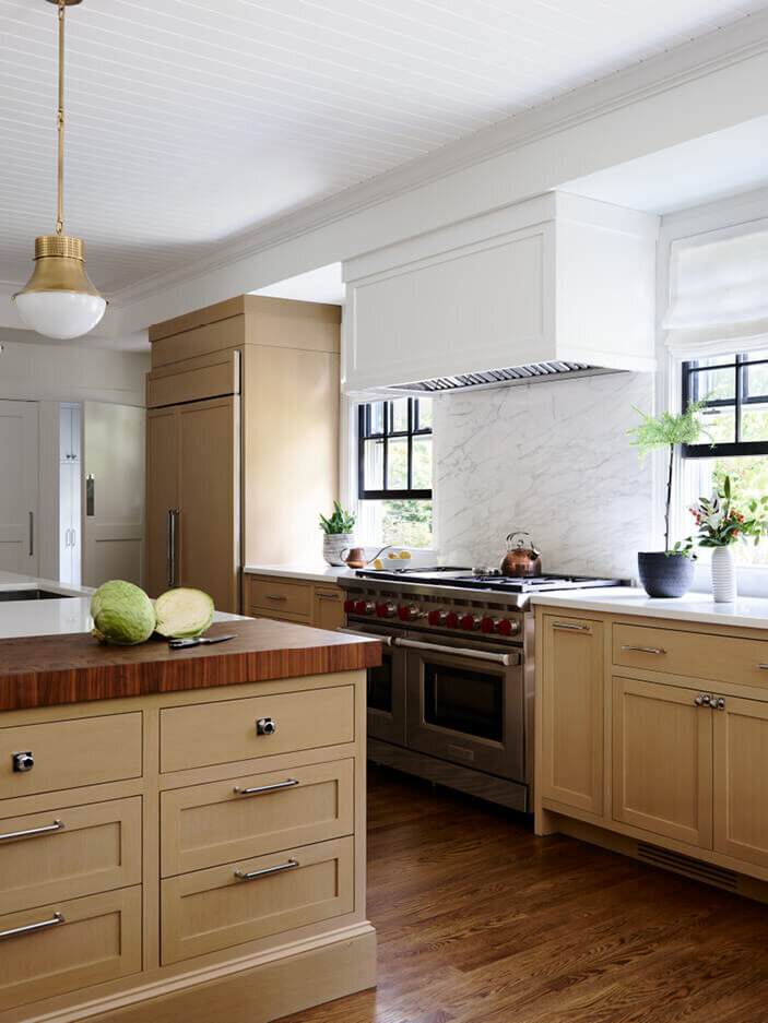 Boston kitchen and bath designer creates natural oak cabinets with white counters and a marble backsplash, blending warmth and elegance for a timeless design.