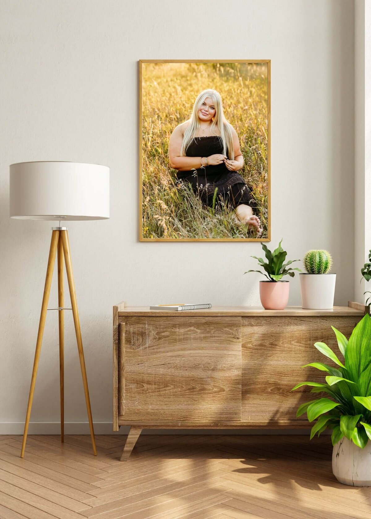 image of artwork of a senior girl in a black dress hanging above a dresser with plants on it