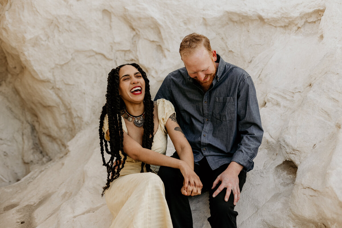 mand and woman sitting on a white rock laughing