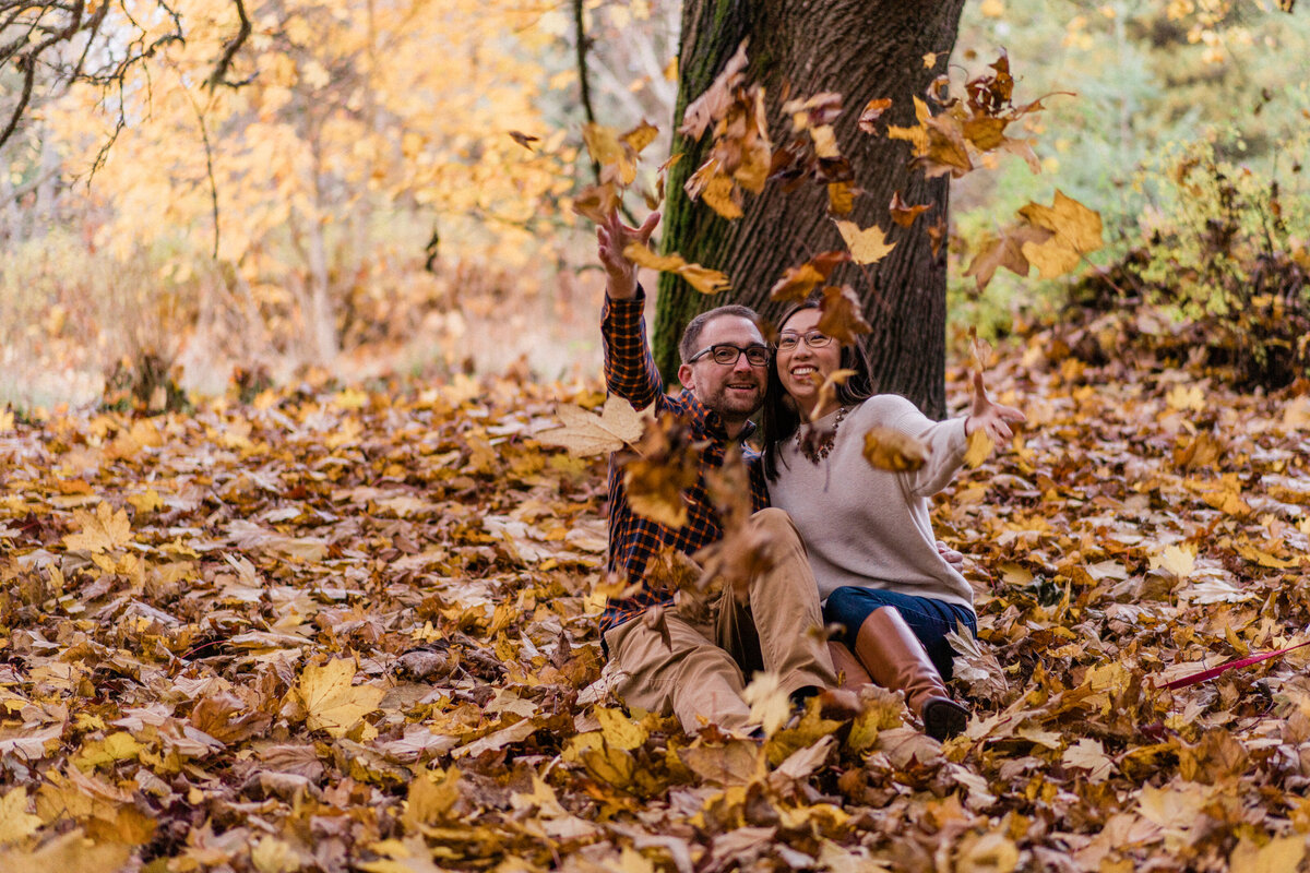 Bride and groom toss fall leaves into the air at best spots for engagement photos in Seattle, Discovery Park, in Magnolia
