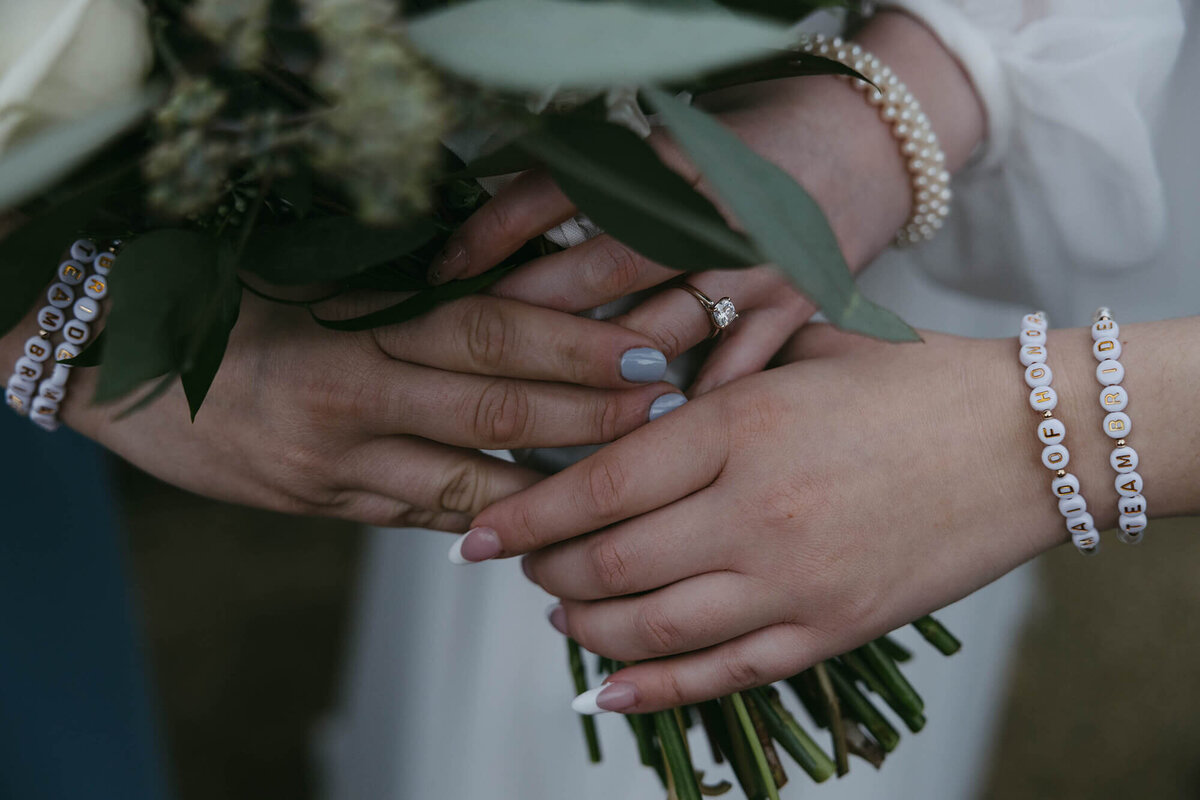 Close up of three female hands holding the stems of a wedding bouquet, showing details of the bracelets they each wear.