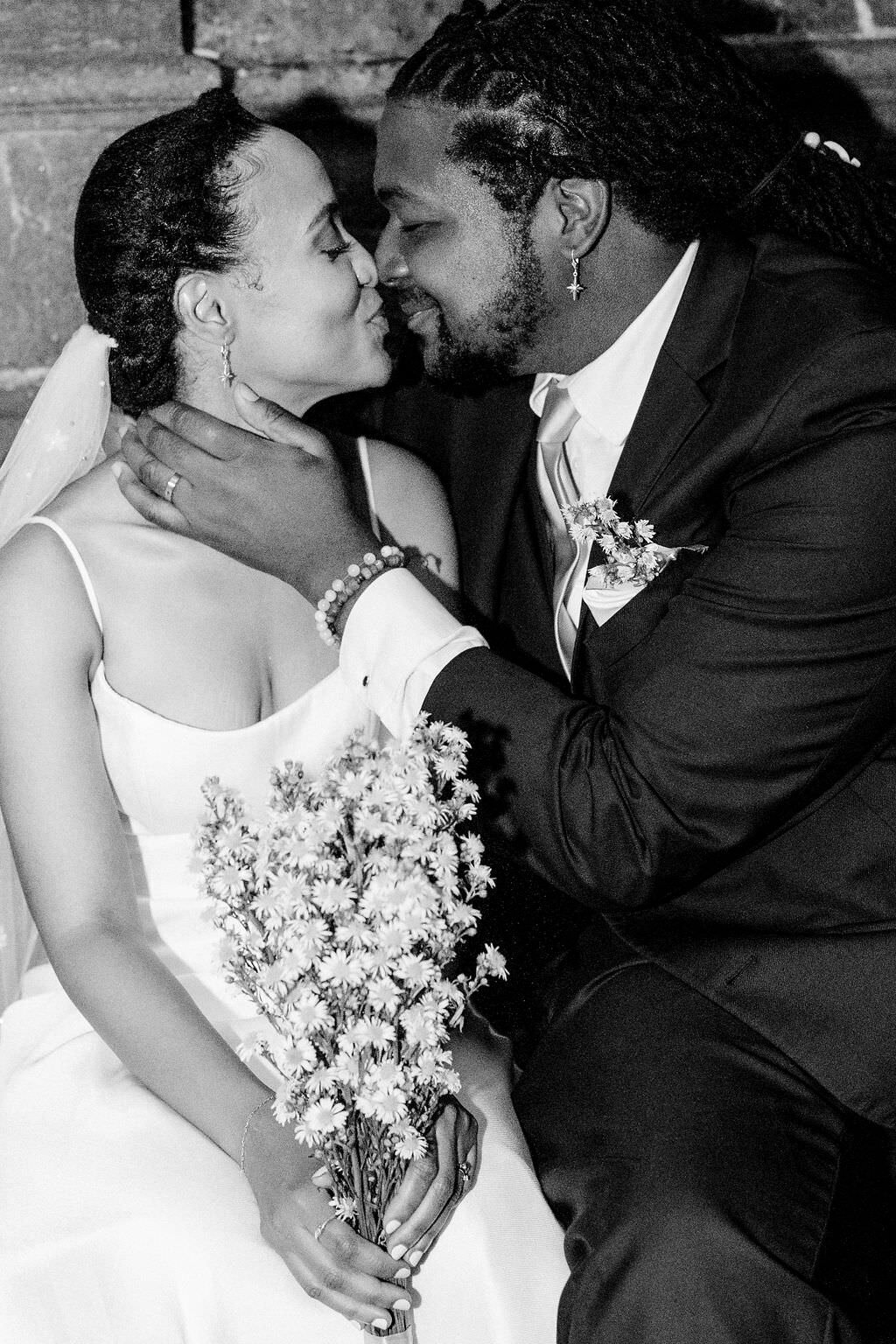 black and white photo of a bride and groom sitting next to each other about to kiss
