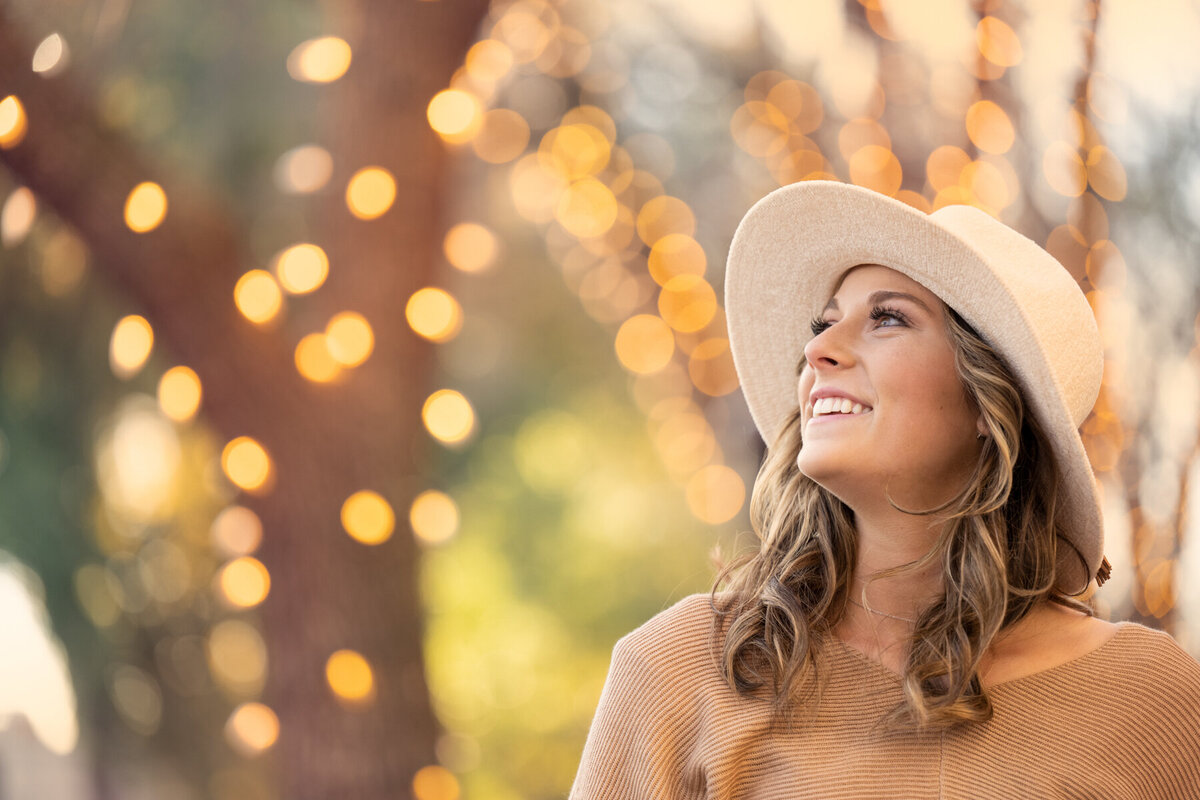 senior picture of Lakeville Minnesota girl wearing a white hat with lights in trees in the city