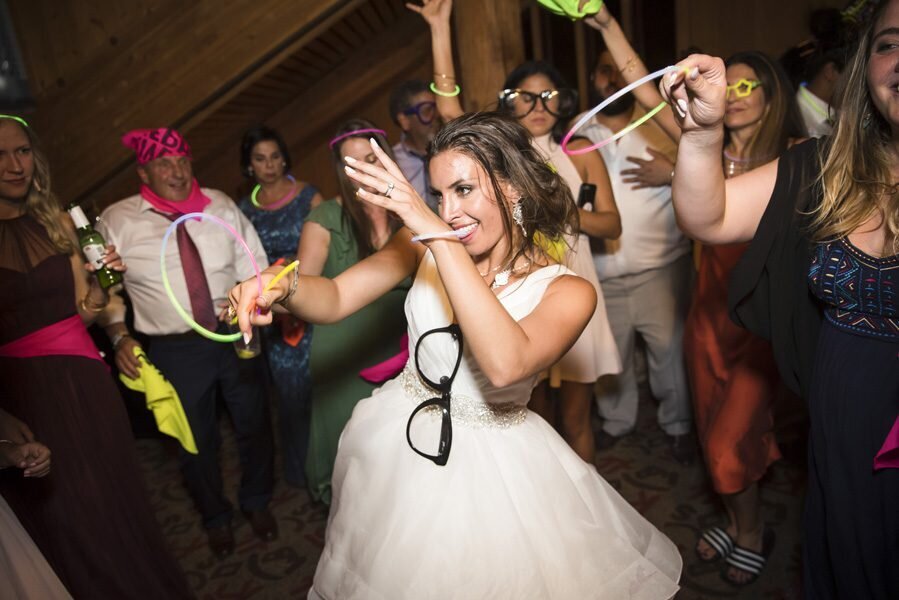 A bride strikes a fun dance pose surrounded by guests holding glow sticks.