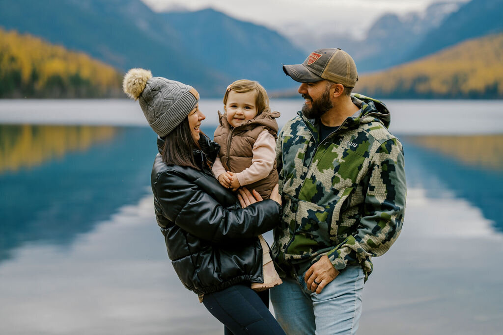 Joseph Mayden smiling with his wife and daughter by a mountain lake in Montana, reflecting his values of family, adventure, and connection through photography.