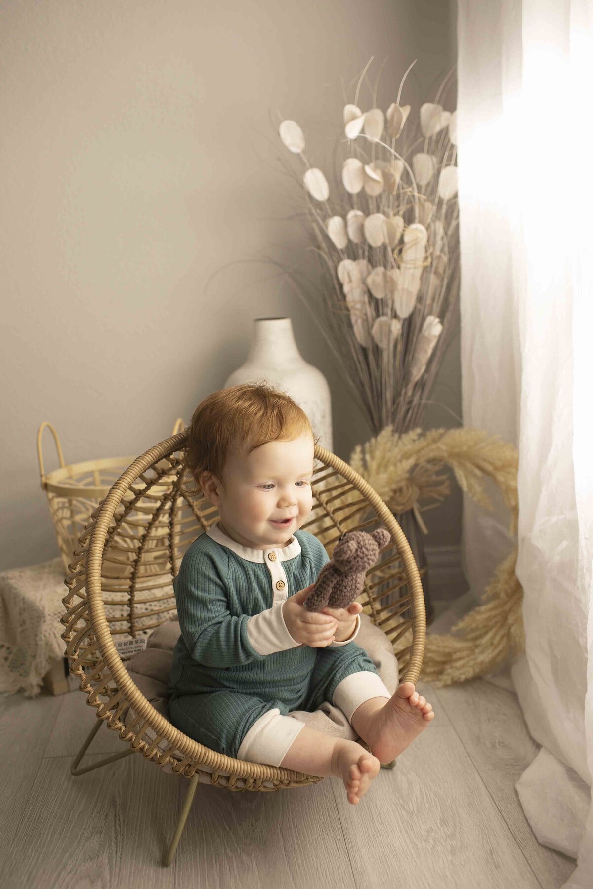 One-year-old birthday boy in a wicker chair, looking playful and joyful as he celebrates his first birthday in the studio