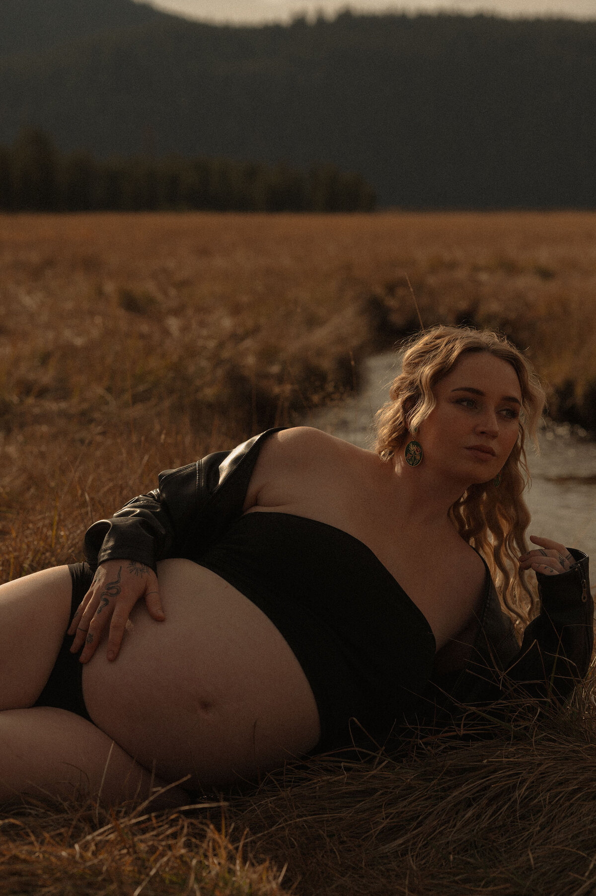 expecting mother places her hand on her belly and lays near a creek in Bend, Oregon