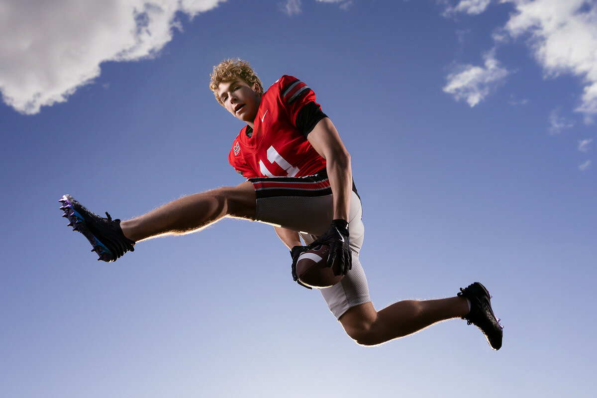 A high school senior in a football uniform jumps mid-air, captured in dramatic senior photos Dallas.
