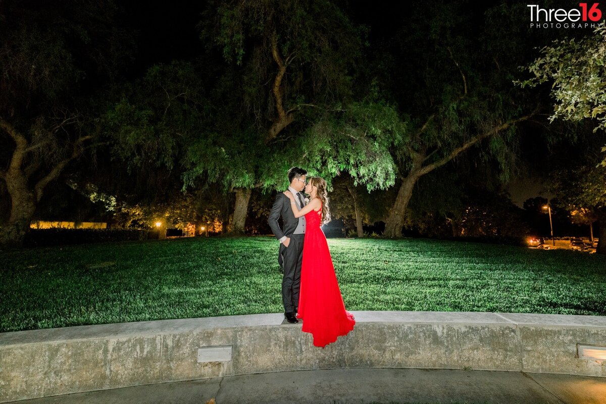 Bride and Groom gaze into each other's eyes during a night shot while standing on a short wall