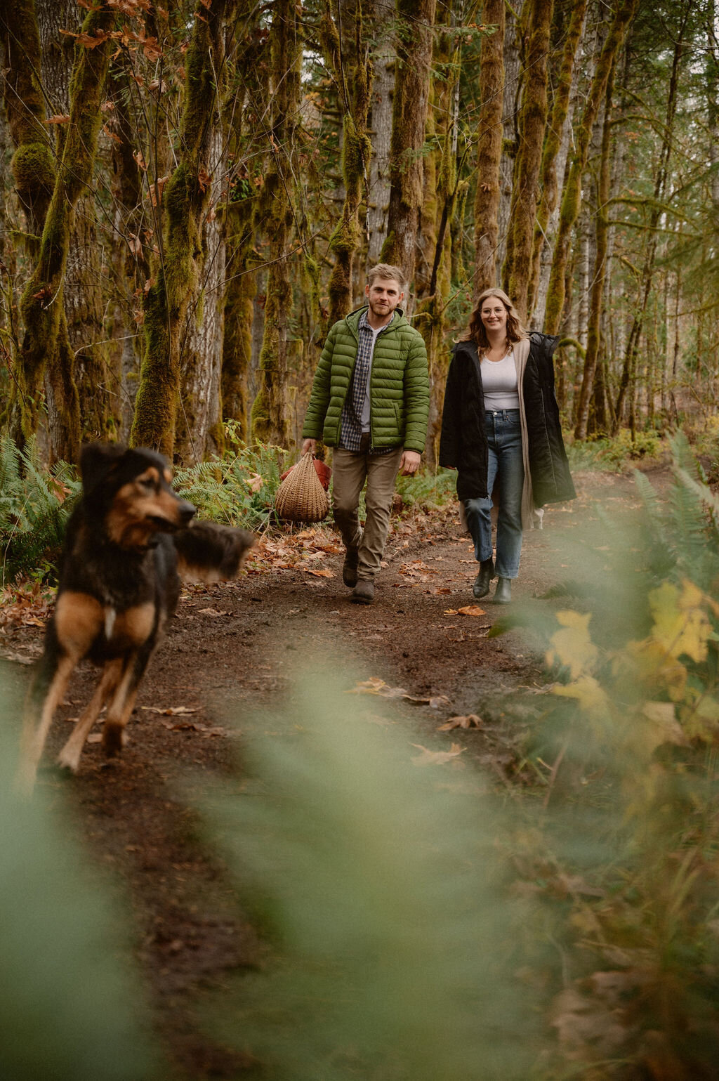 couple walking in trail with a dog running in front