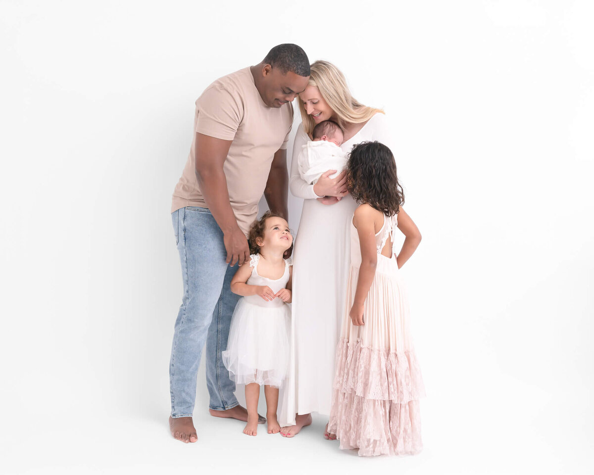 beautiful family with small children and newborn against white backdrop in full length candid portrait
