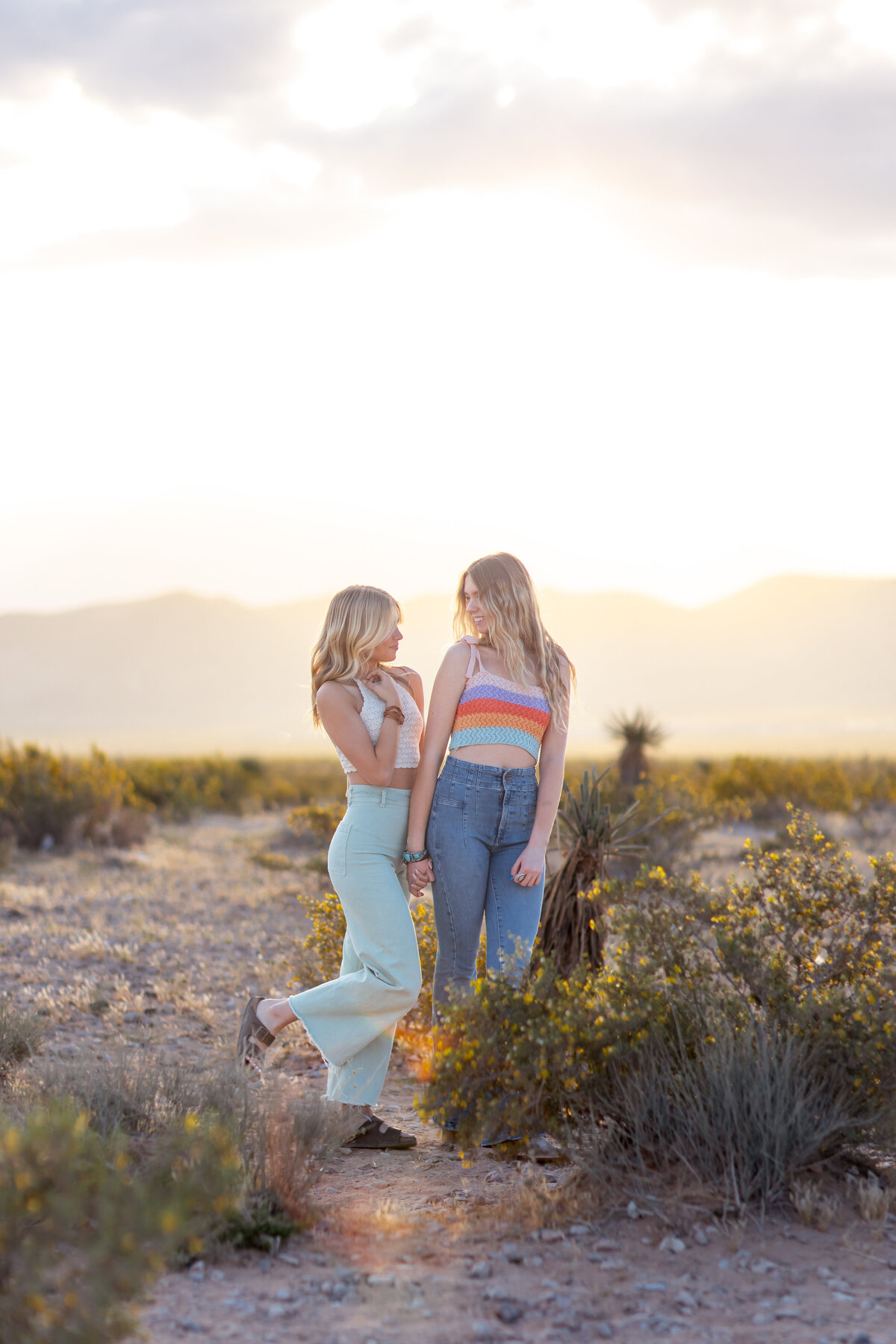 Graduating seniors and best friends laughing together at sunrise during a playful Brooke Tucker photography session at Seven Magic Mountain near Las Vegas