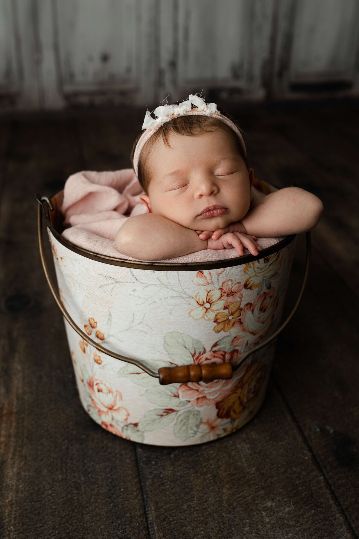baby girl sleeping with her head on her hands in a floral bucket and headband for her york newborn photos