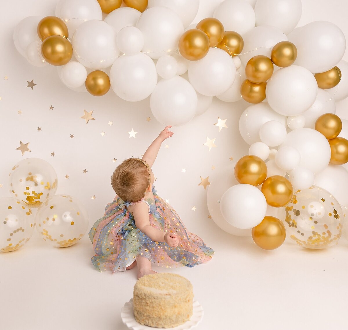 baby girl pointing to gold and white balloons in portland studio session