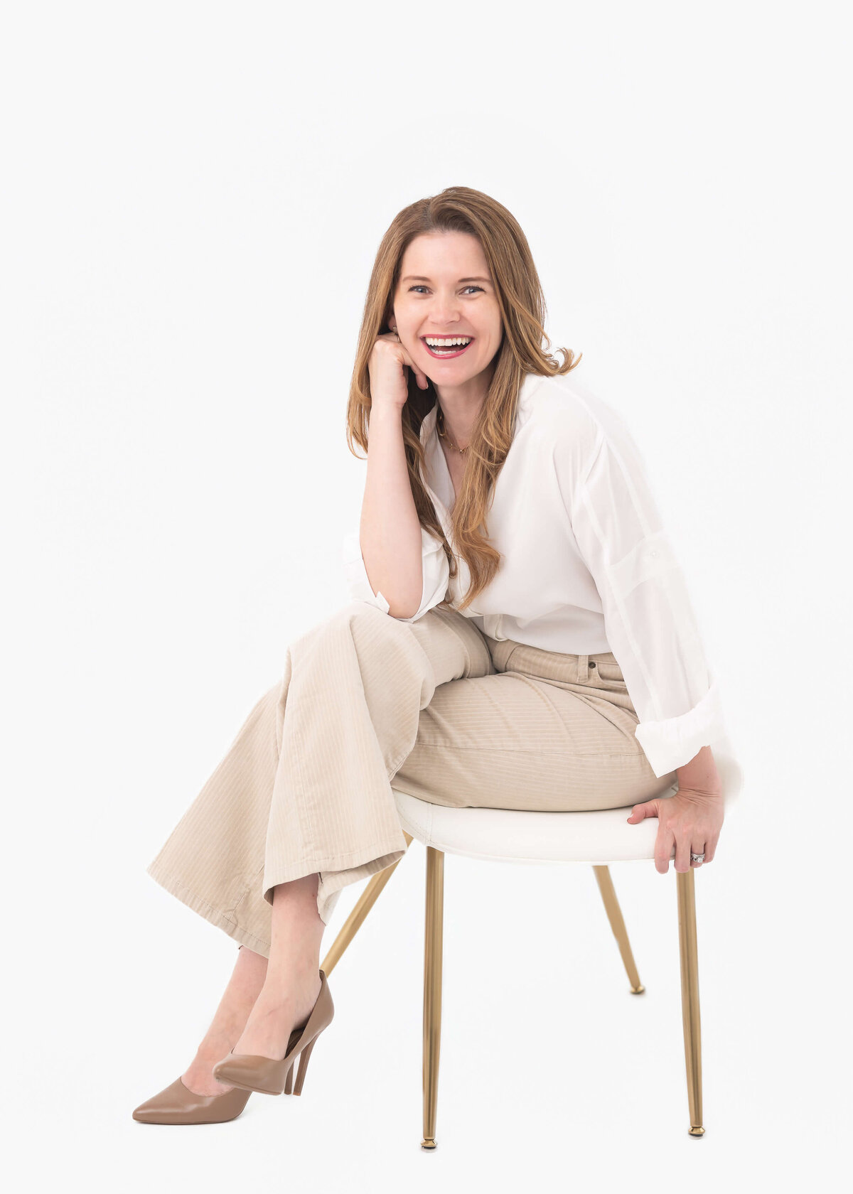 attractive business woman in white blouse and beige pants sitting sideways on white chair in white studio, captured by Allison Amores Photography 