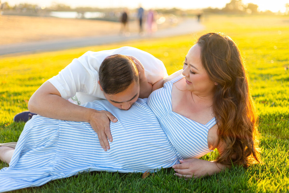 Partner kisses baby bump while woman reclines on grass during golden hour — Bay Area Maternity Portfolio - Ellobelle Photography Family Photographer