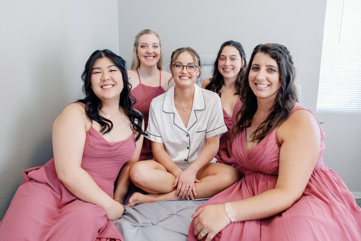 wedding photographer bay area photographs bride sitting on a bed in a bridal suite with her four bridesmaids who are in blush pink bridesmaid dresses